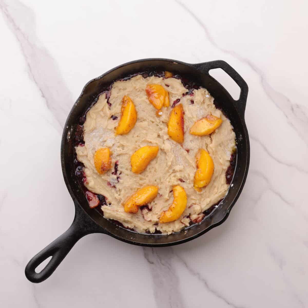 A skillet with the assembled cobbler in it, ready to bake.