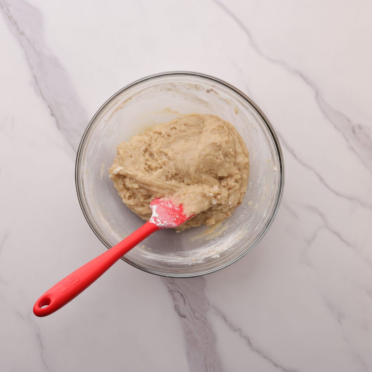 A glass bowl with the mixed batter and a red spatula.