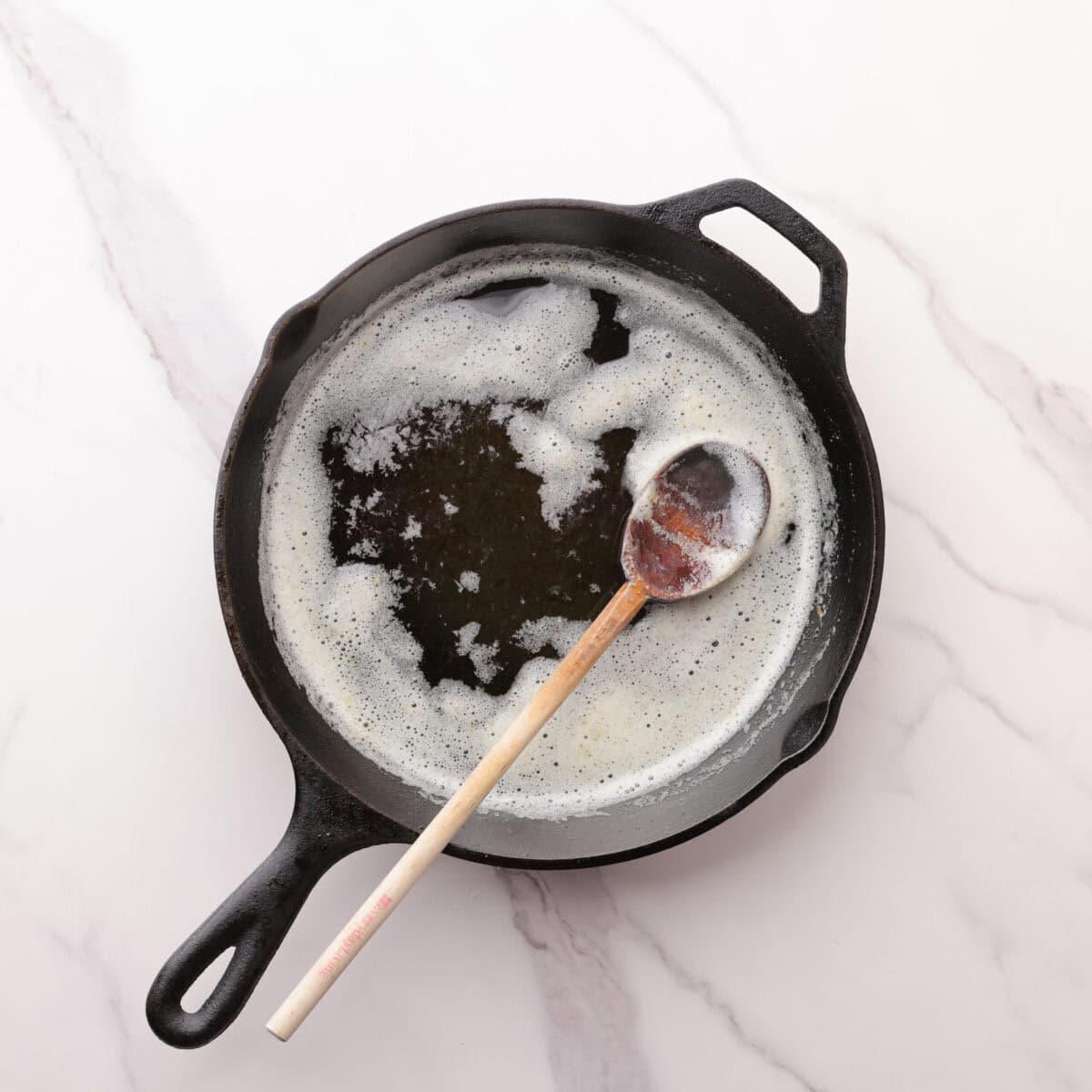A skillet with browned butter and a wooden spoon in it for stirring.