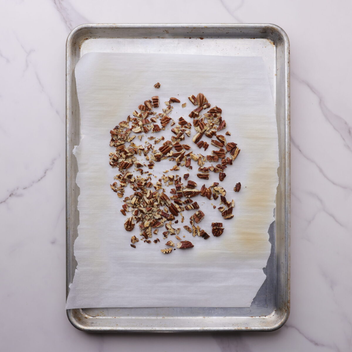 A cookie tray with chopped, roasted pecans on a piece of parchment paper. 