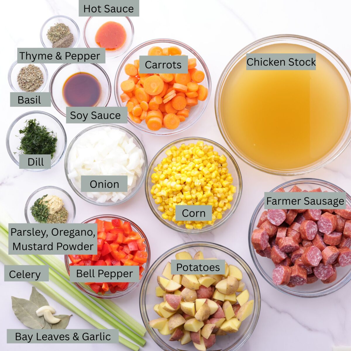 A visual display of the ingredients for Sausage and Pepper soup - hot sauce, soy sauce, thyme, pepper, basil dill, parsley, oregano, mustard powder, onion, celery, carrots, corn, potatoes, farmer sausage, chicken stock, garlic cloves and bay leaves - each in their own bowl.