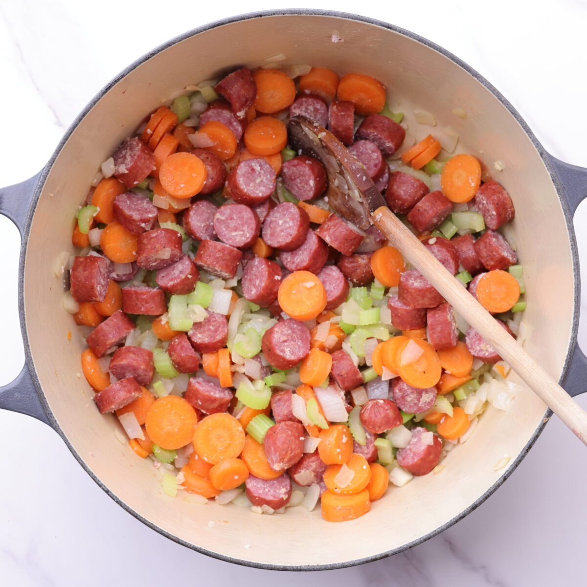 An enameled cast iron pot filled with farmer sausage, carrots, celery, onions and garlic - all gently sauteed.