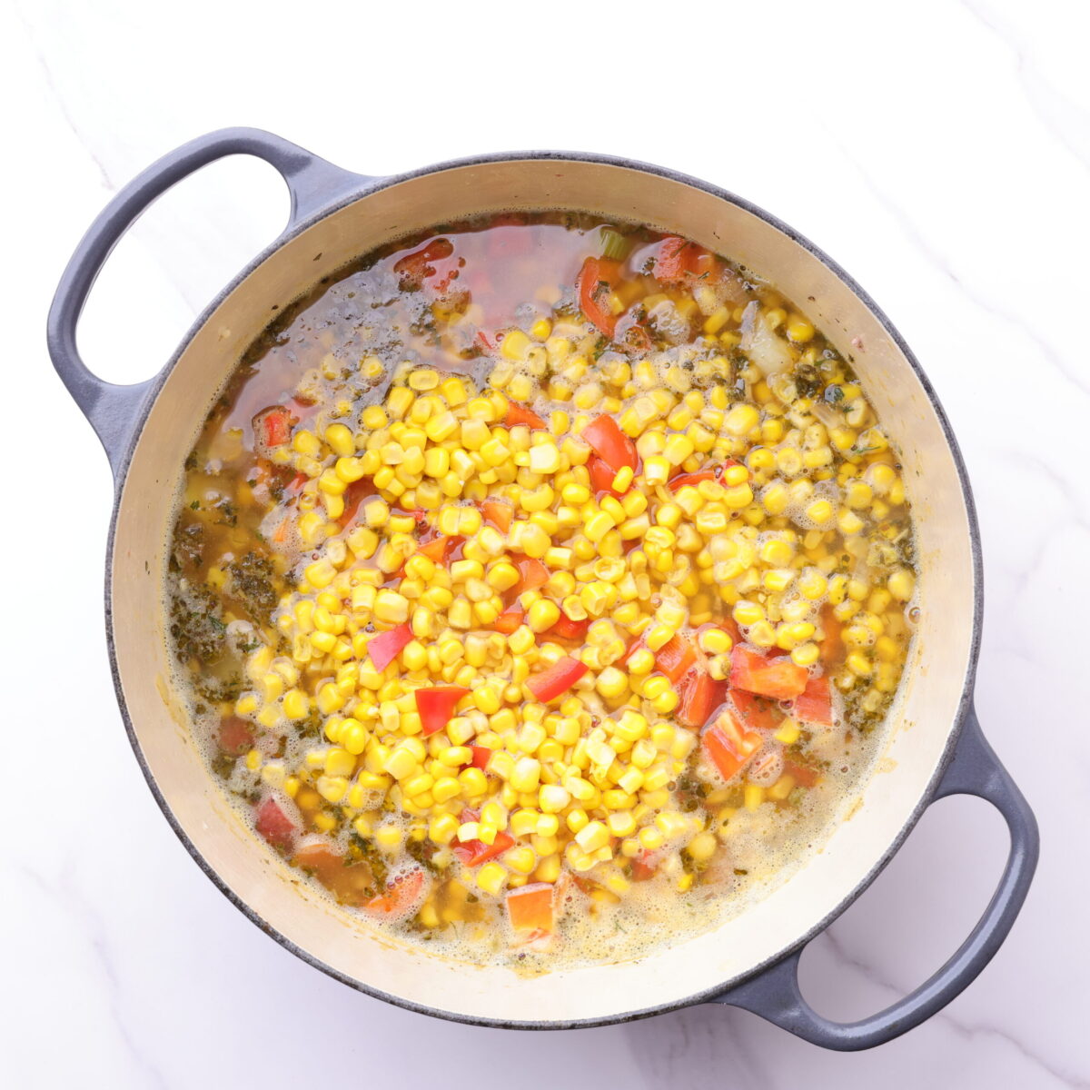 An enameled cast iron pot with all the ingredients in it for the sausage and pepper soup, ready to cook for the last portion of time.