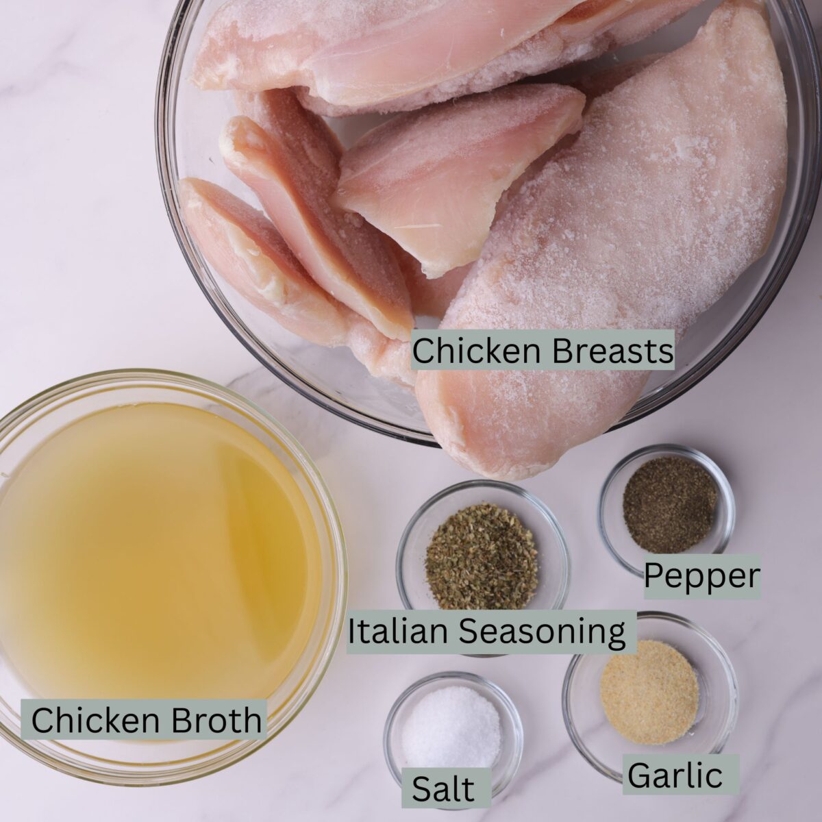 A visual display of the ingredients - frozen chicken breasts, chicken stock, Italian seasoning, garlic powder, salt and pepper - each in their own bowl.