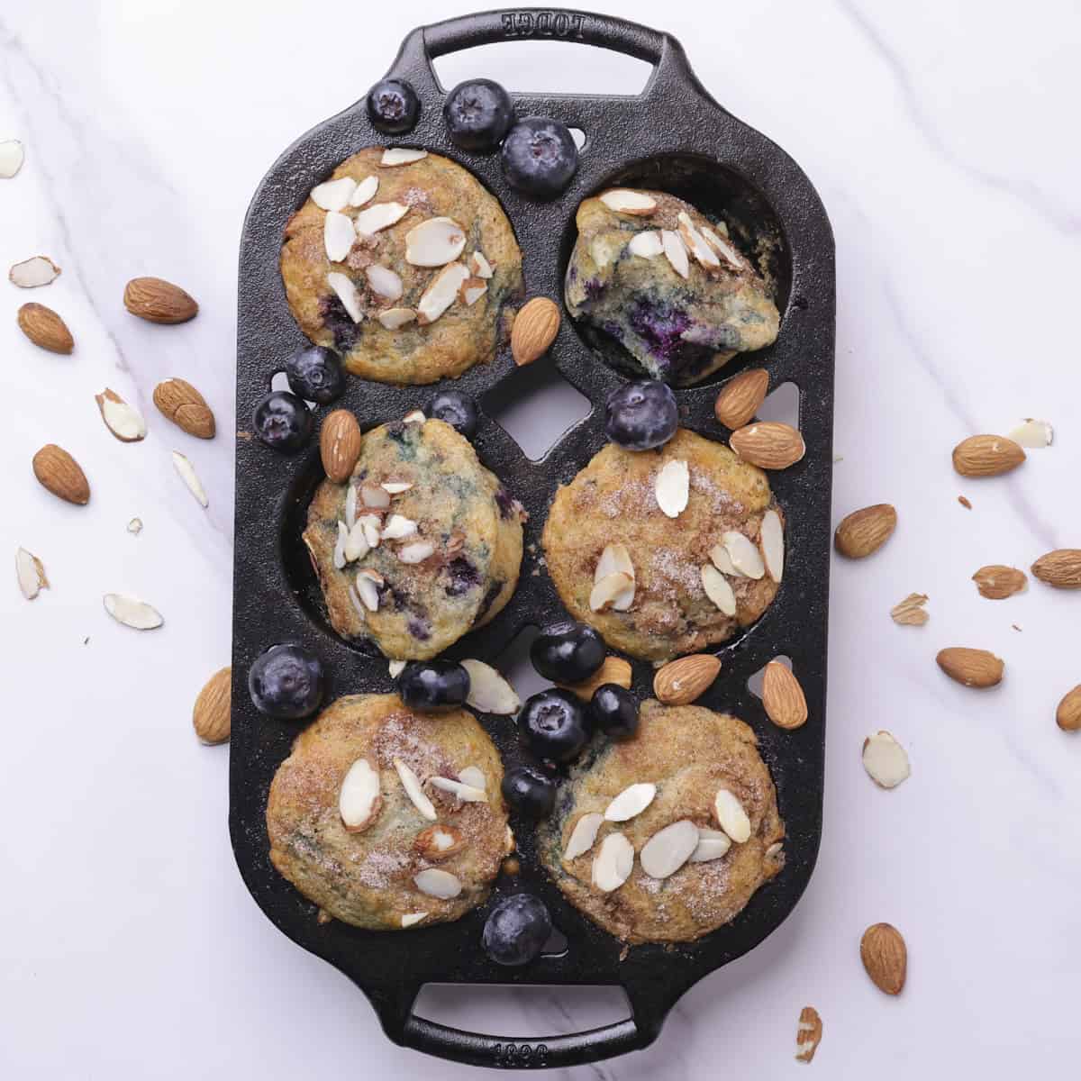 The Blueberry Muffins using Greek Yogurt baked to golden perfection in the cast iron muffin tin, with some on their side in the tin for display.