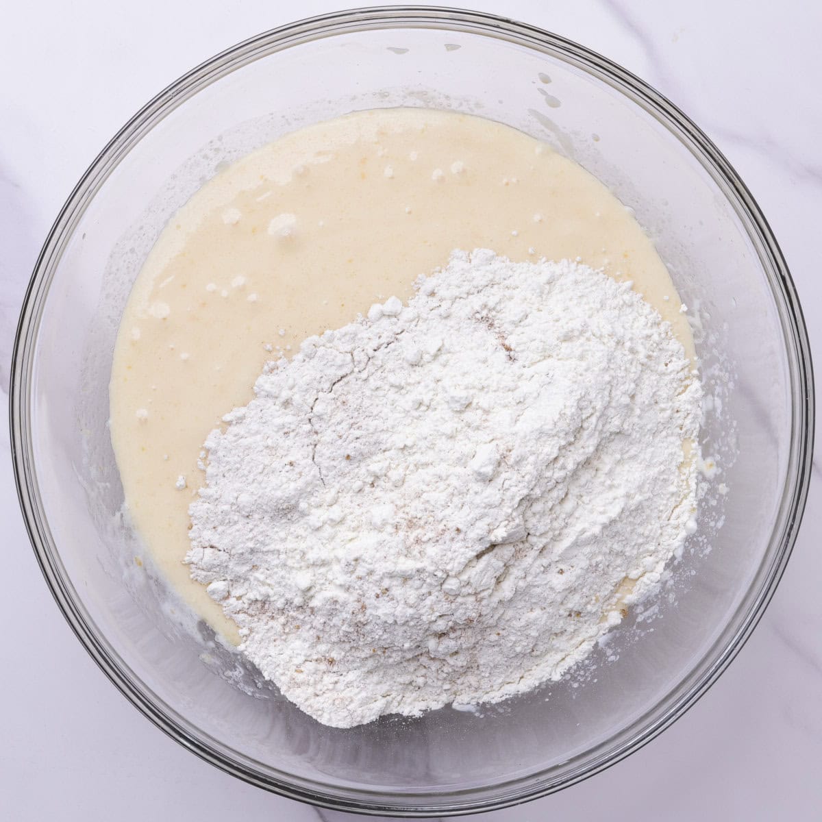 A glass bowl with the dry ingredients resting on top of the wet ingredients, ready to be mixed together.