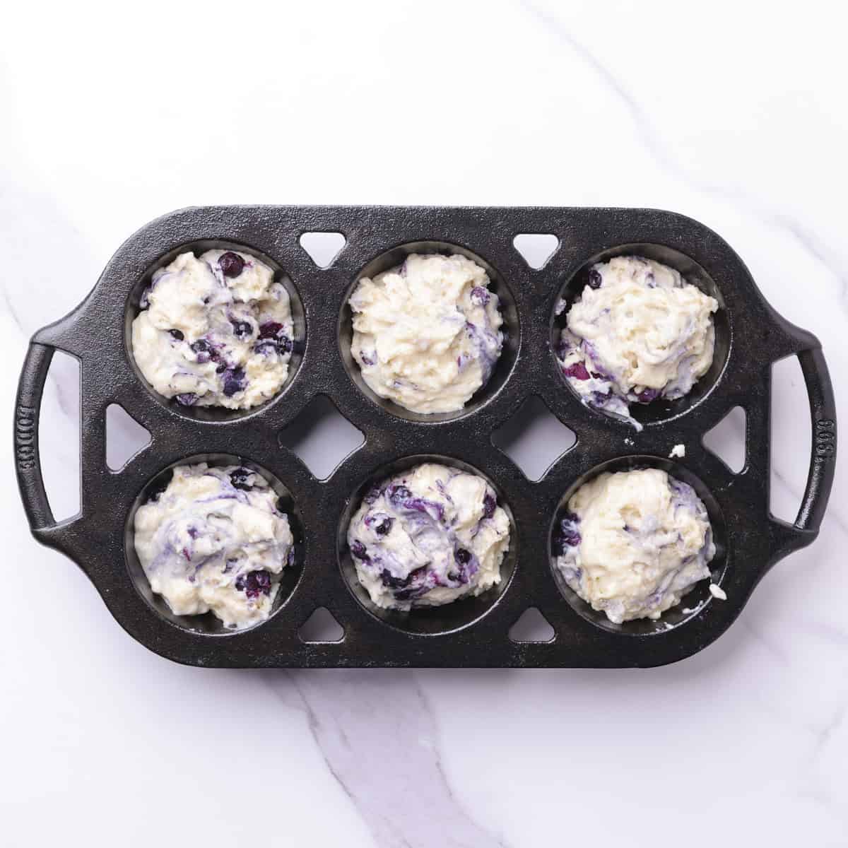 The blueberry muffin with greek yogurt bater divided into the bast iron muffin tin.