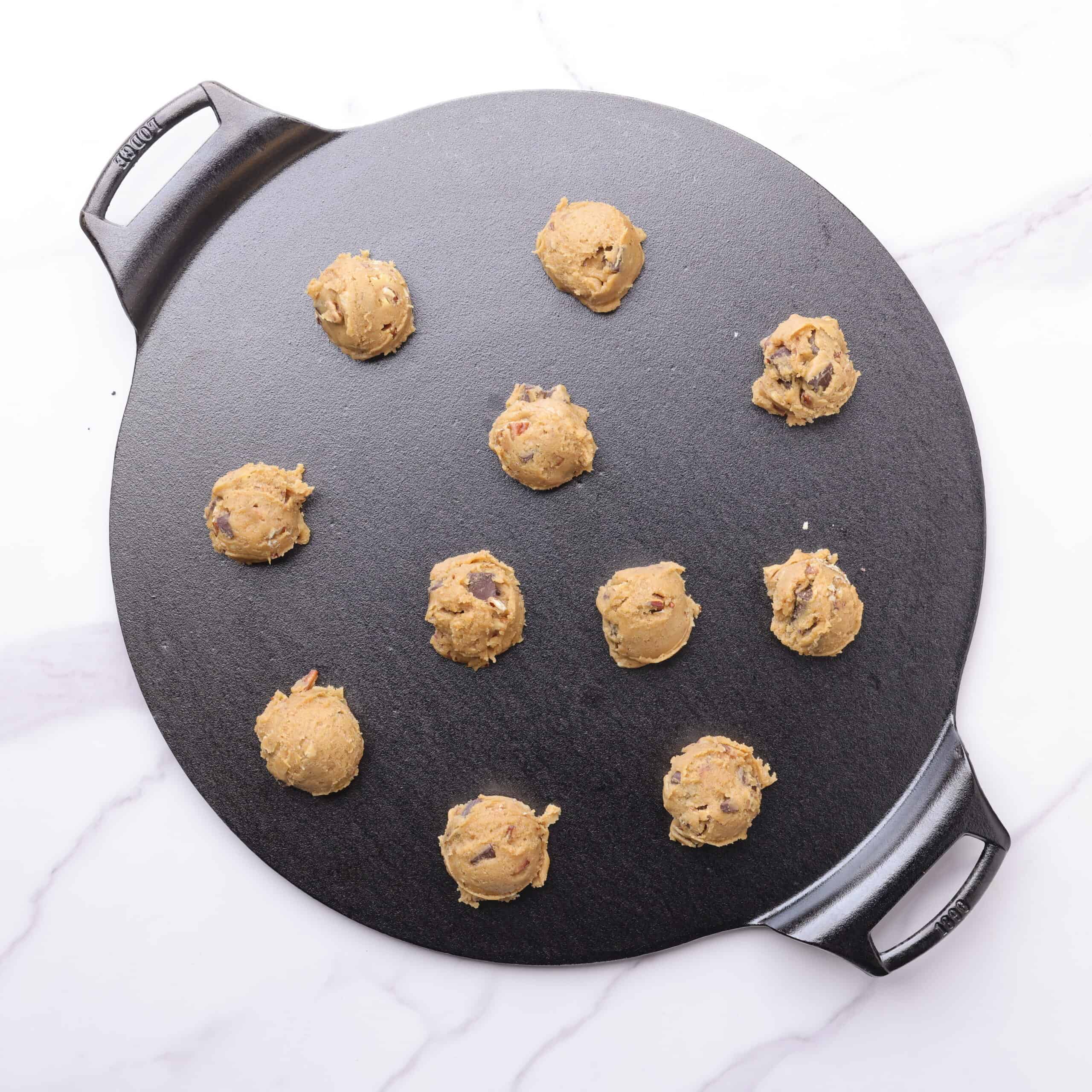 A cast iron baking pan with scoops of chocolate chunk pecan cookie dough arranged on it.