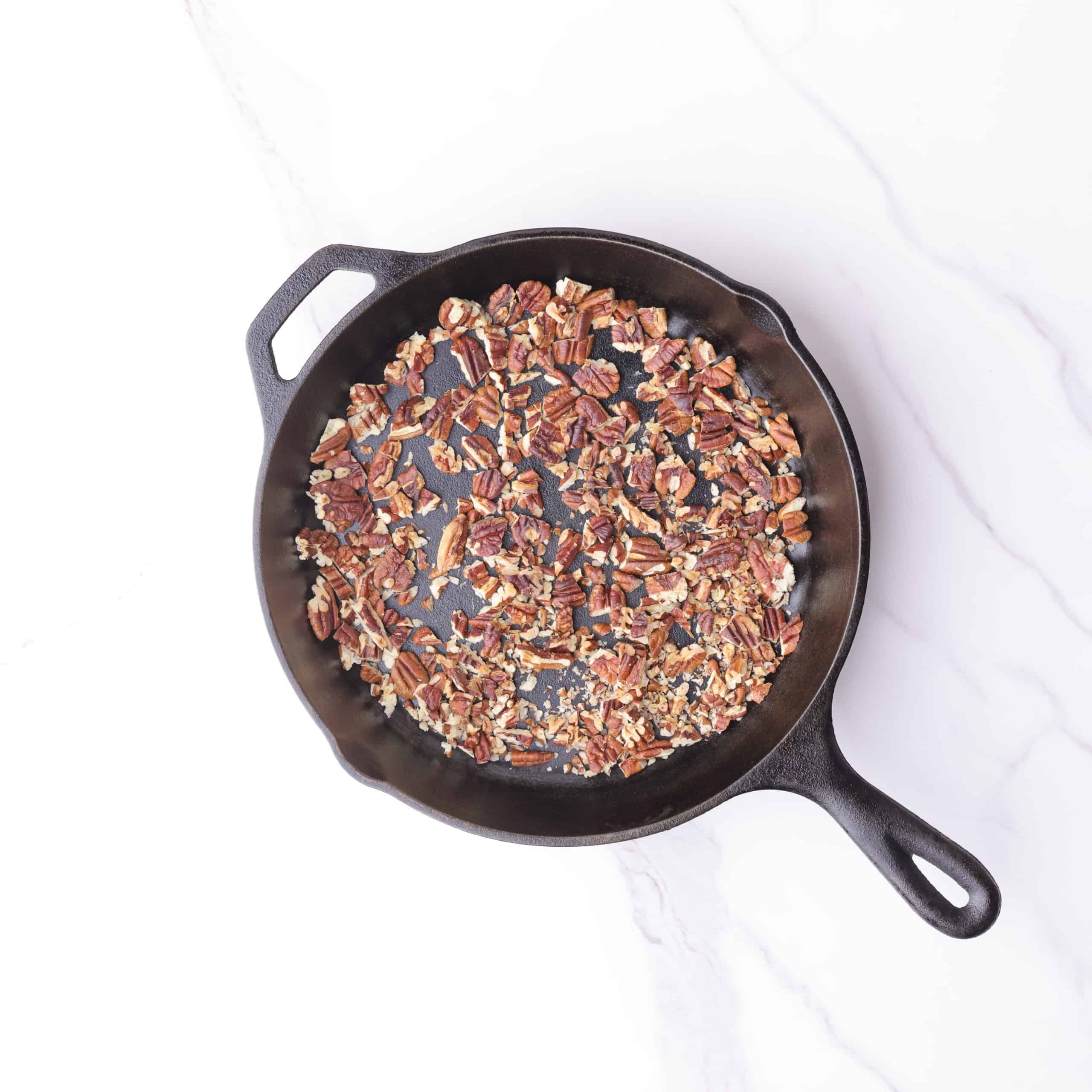 A skillet with roasted, chopped pecans in it.