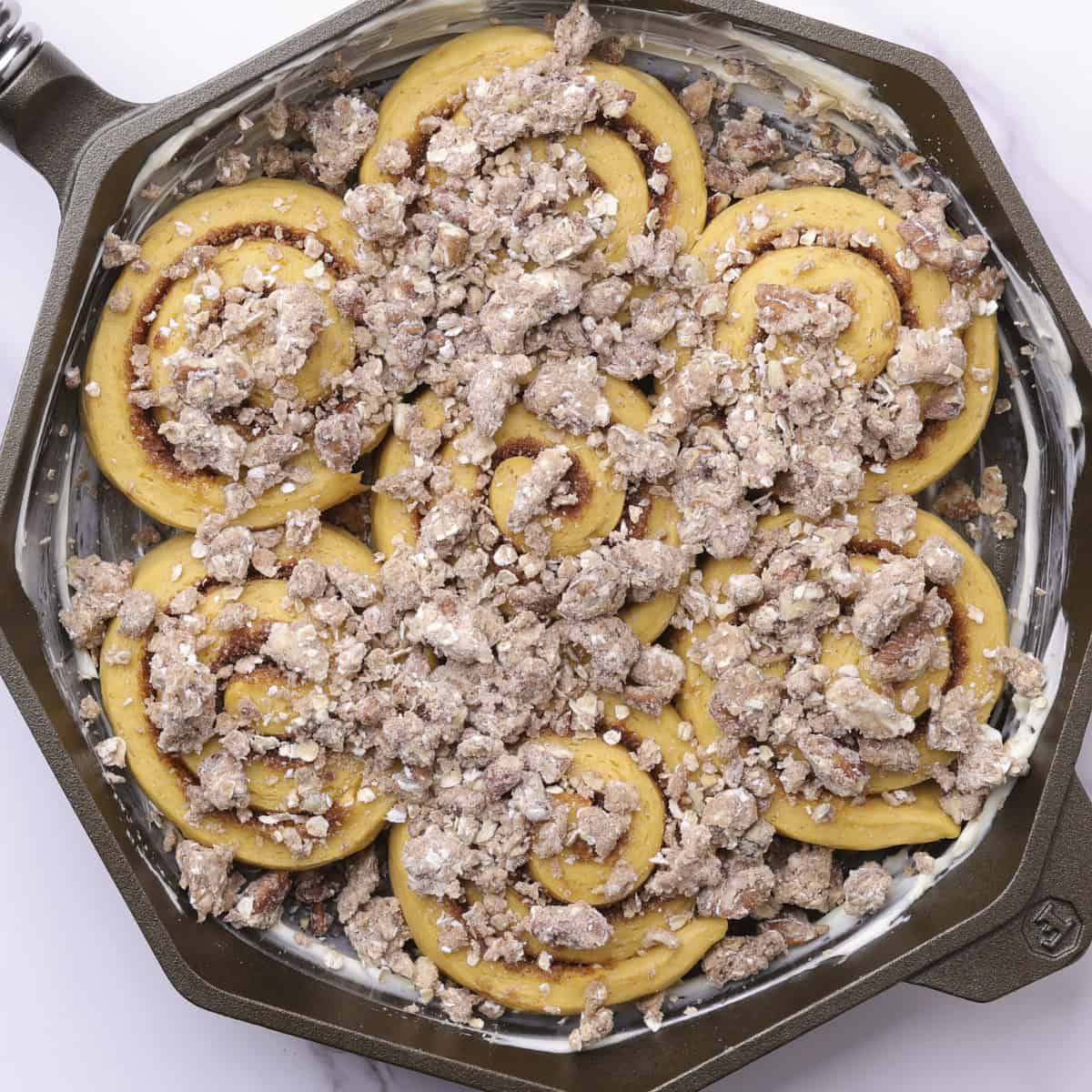 A buttered skillet with the risen pumpkin cinnamon rolls in it, now topped with streusel and ready to bake.