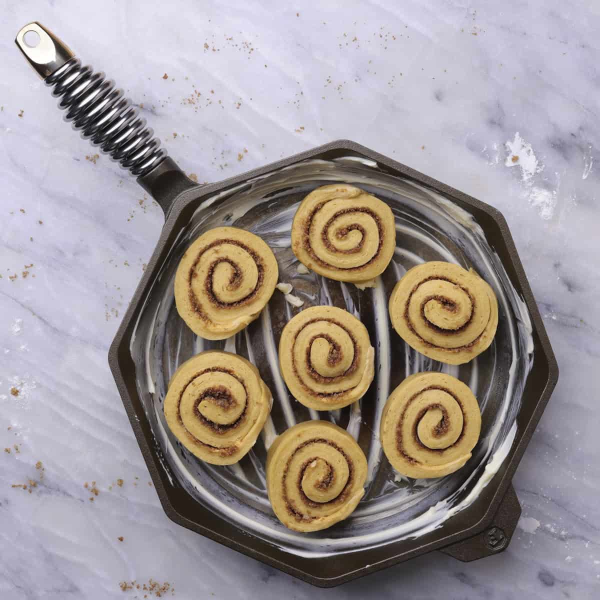 A buttered skillet with 7 rolls arranged in it, ready to rise.