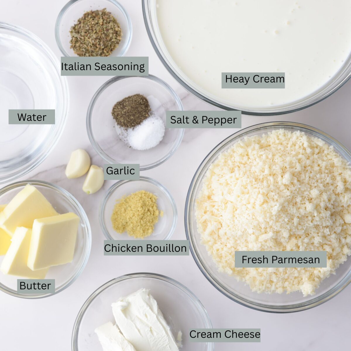 A visual display of the ingredients for the homemade alfredo sauce - heavy cream, grated Parmesan cheese, butter, cream cheese, water, garlic, Italian seasoning, chicken bullion and salt and pepper - each in their own bowl.   