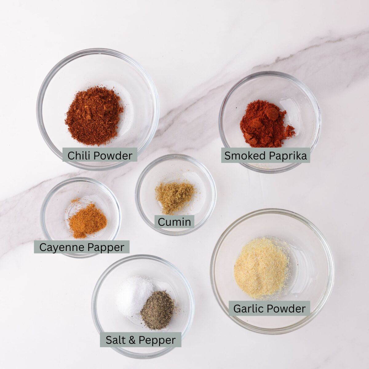 A visual display of the ingredients in the blackened seasoning with each spice, chili powder, smoked paprika, cumin, cayenne, garlic powder, and salt and pepper in it's own bowl.