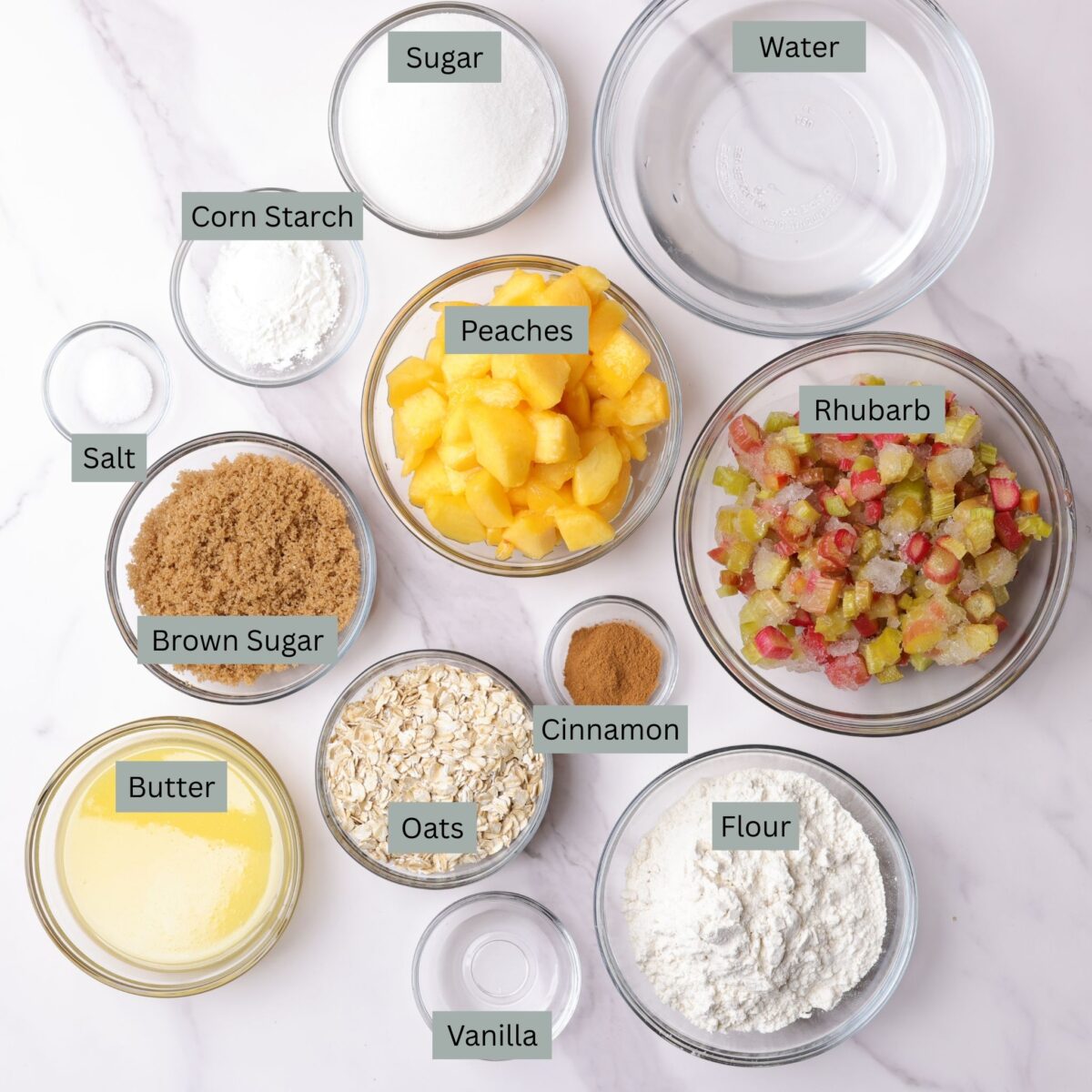 A visual display of the ingredients - granulated sugar, cornstarch, water, salt, brown sugar, peaches, rhubarb, cinnamon, oats, melted butter, flour and vanilla - each in their own bowl.