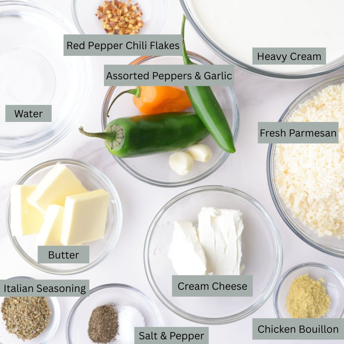 A visual display of the ingredients for the homemade alfredo sauce - heavy cream, grated Parmesan cheese, butter, cream cheese, water, garlic and a variety of spicy peppers (jalapeño, habanero and serrano), Italian seasoning, chicken bullion, red pepper chili flakes and salt and pepper - each in their own bowl.   