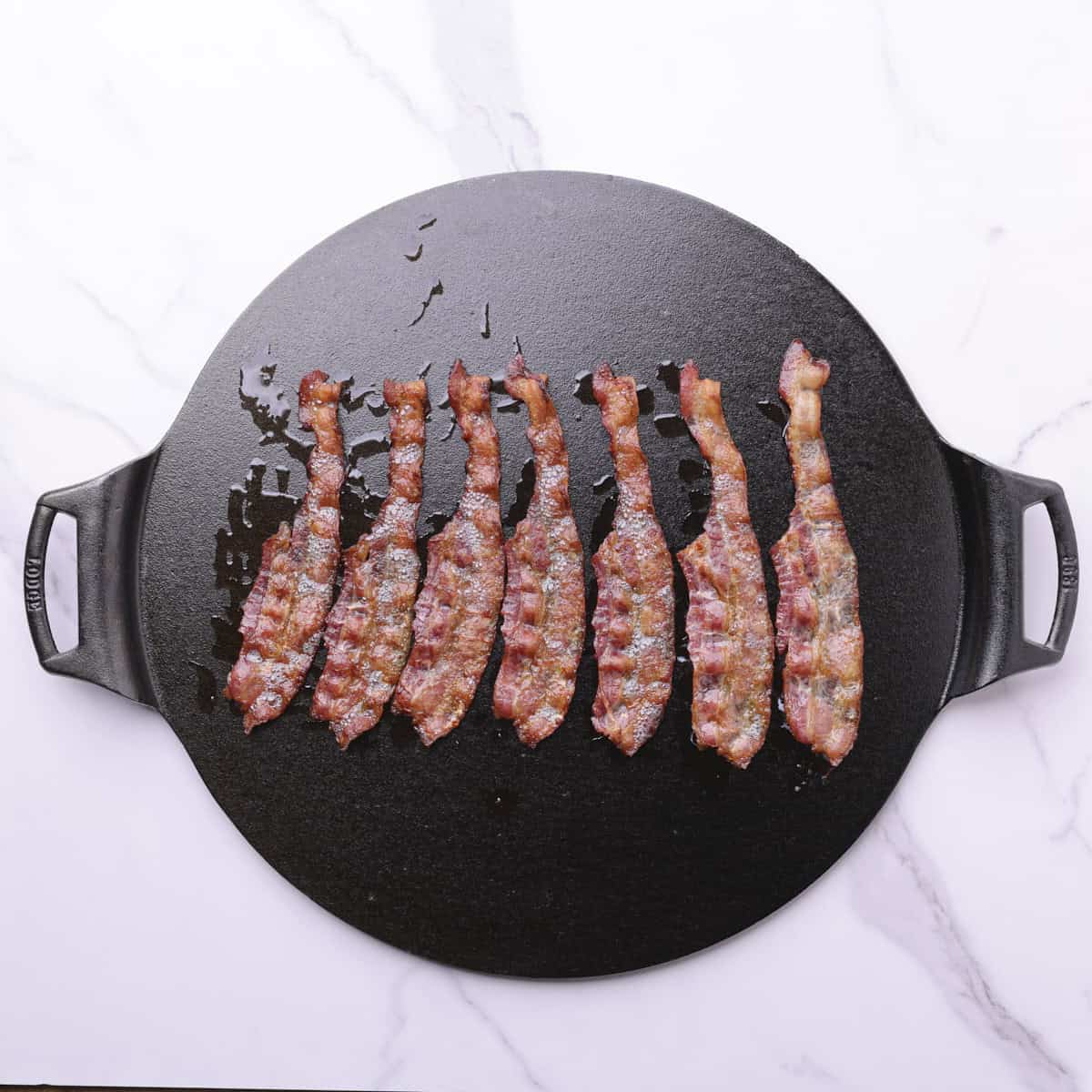 A cast iron pan with strips of cooked bacon on it.