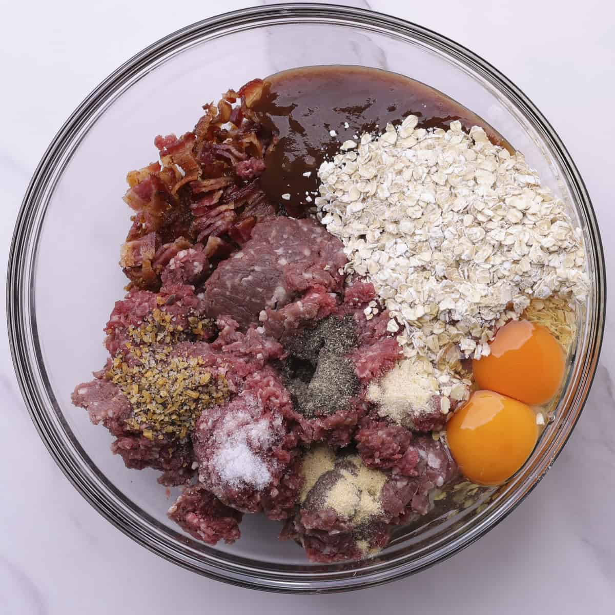 A glass bowl with all the ingredients needed for the moose burgers in it prior to mixing.