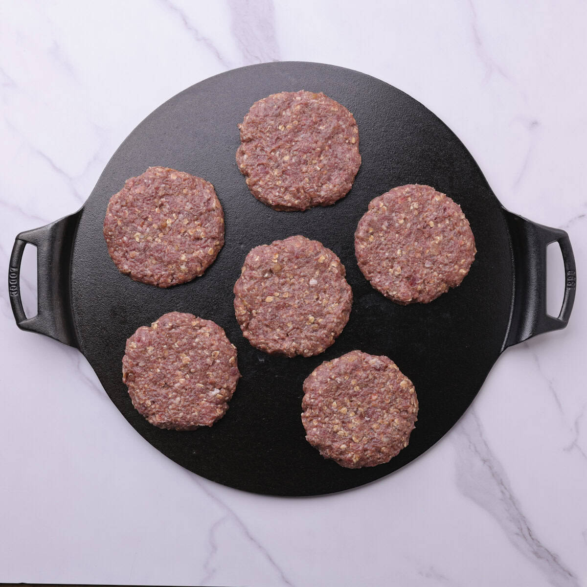 Six raw moose patties formed and placed on a cast iron pan.