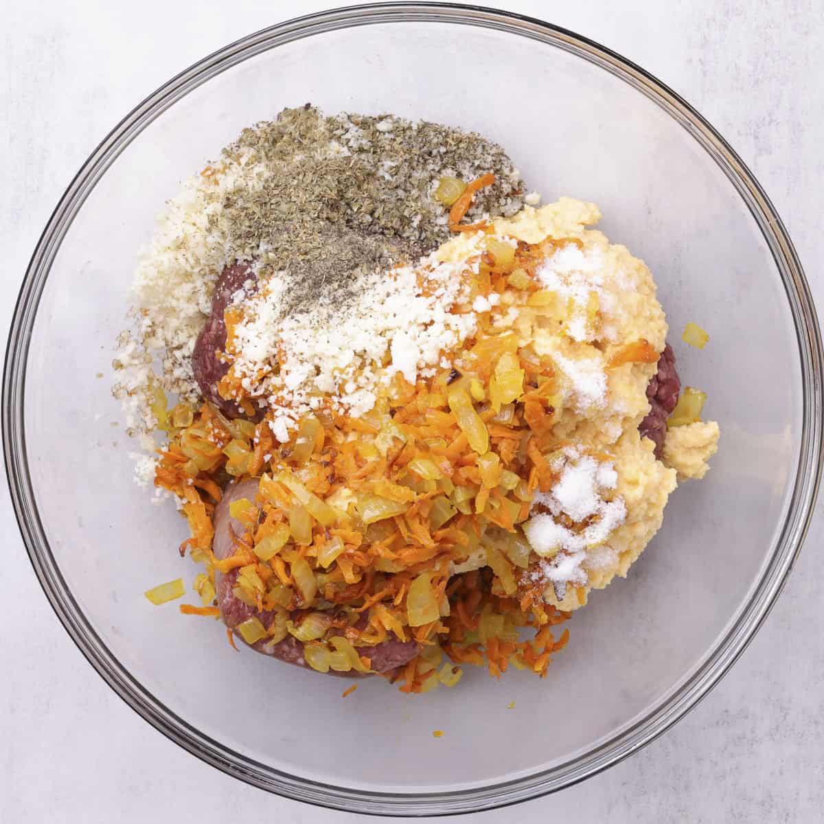 The meat, onion and carrot mixture, breadcrumb mixture and spices in a glass bowl.