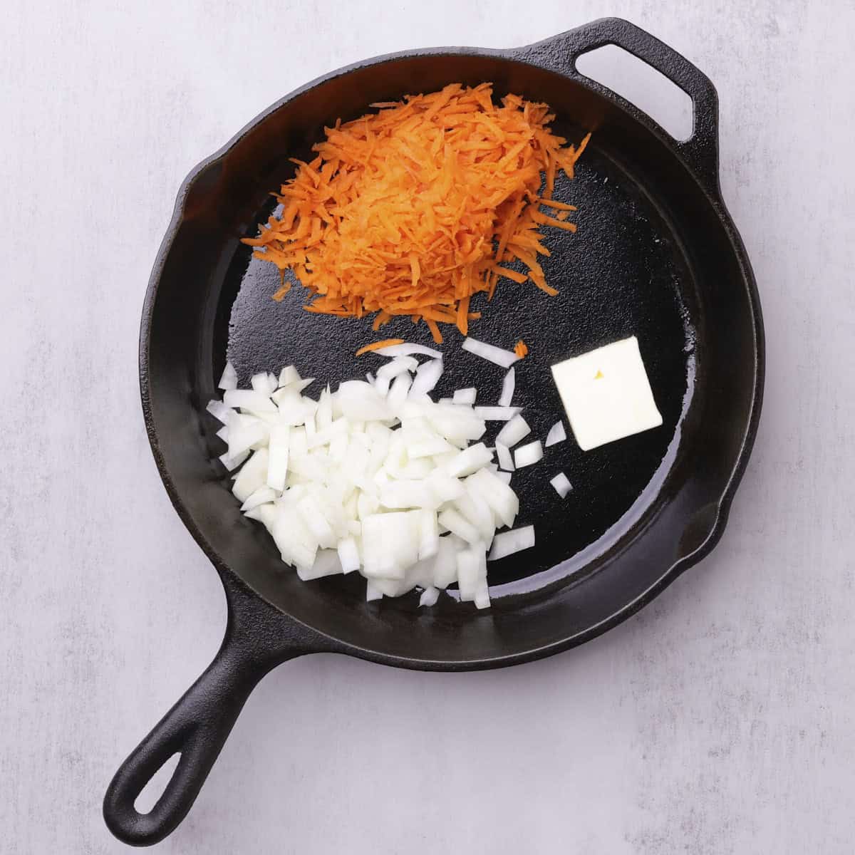 A skillet with the shredded carrots, chopped onions and butter in it, ready to saute.