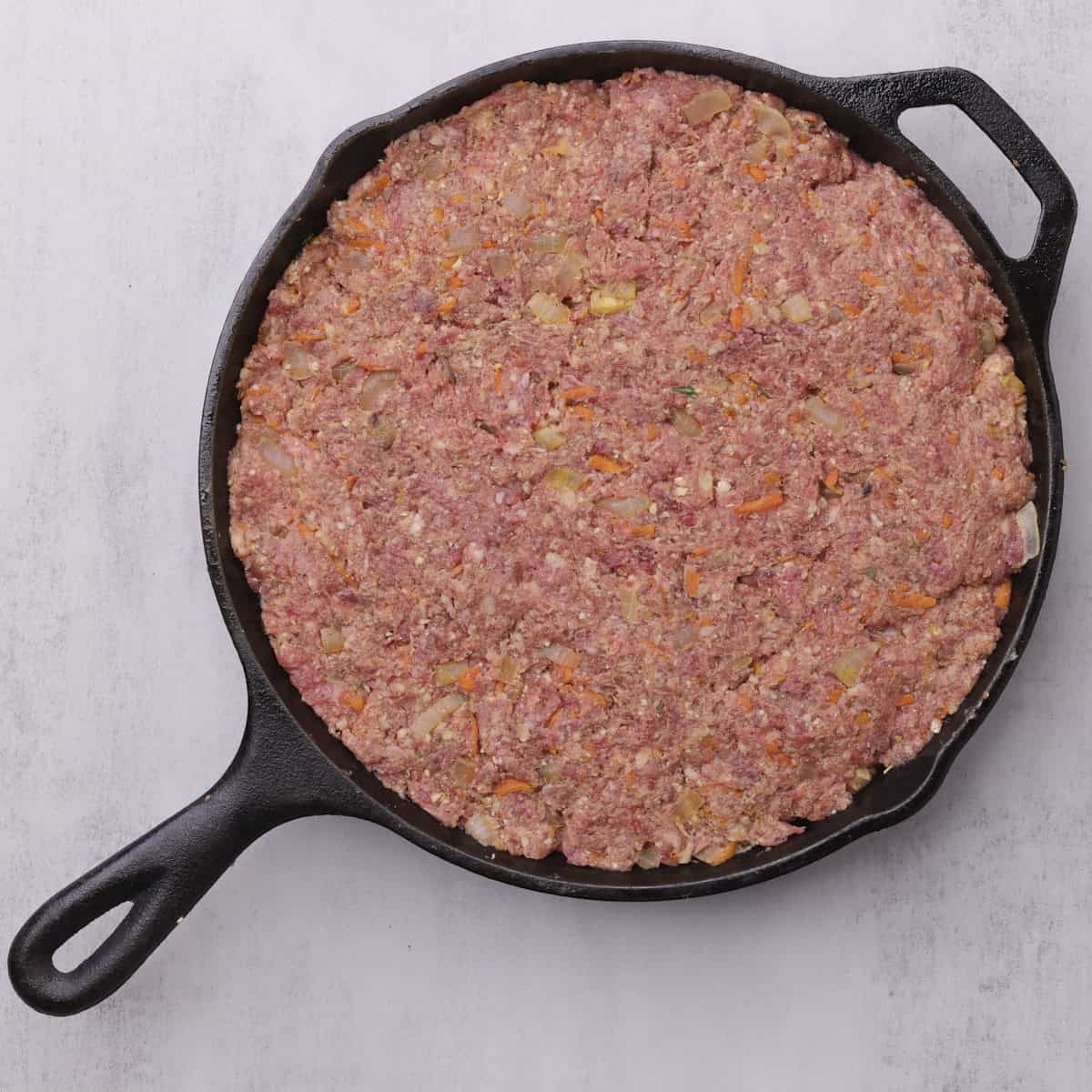 The skillet with the meatloaf topped with the remaining meat mixture and ready to bake.