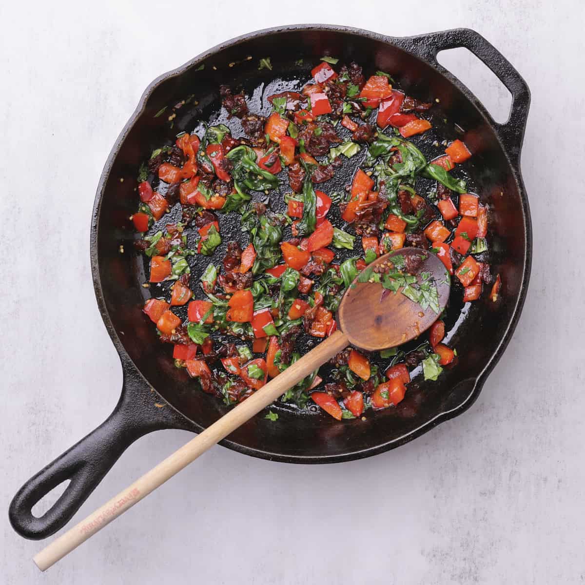 A skillet with the sauteed veggie mixture in it and a wooden spoon.
