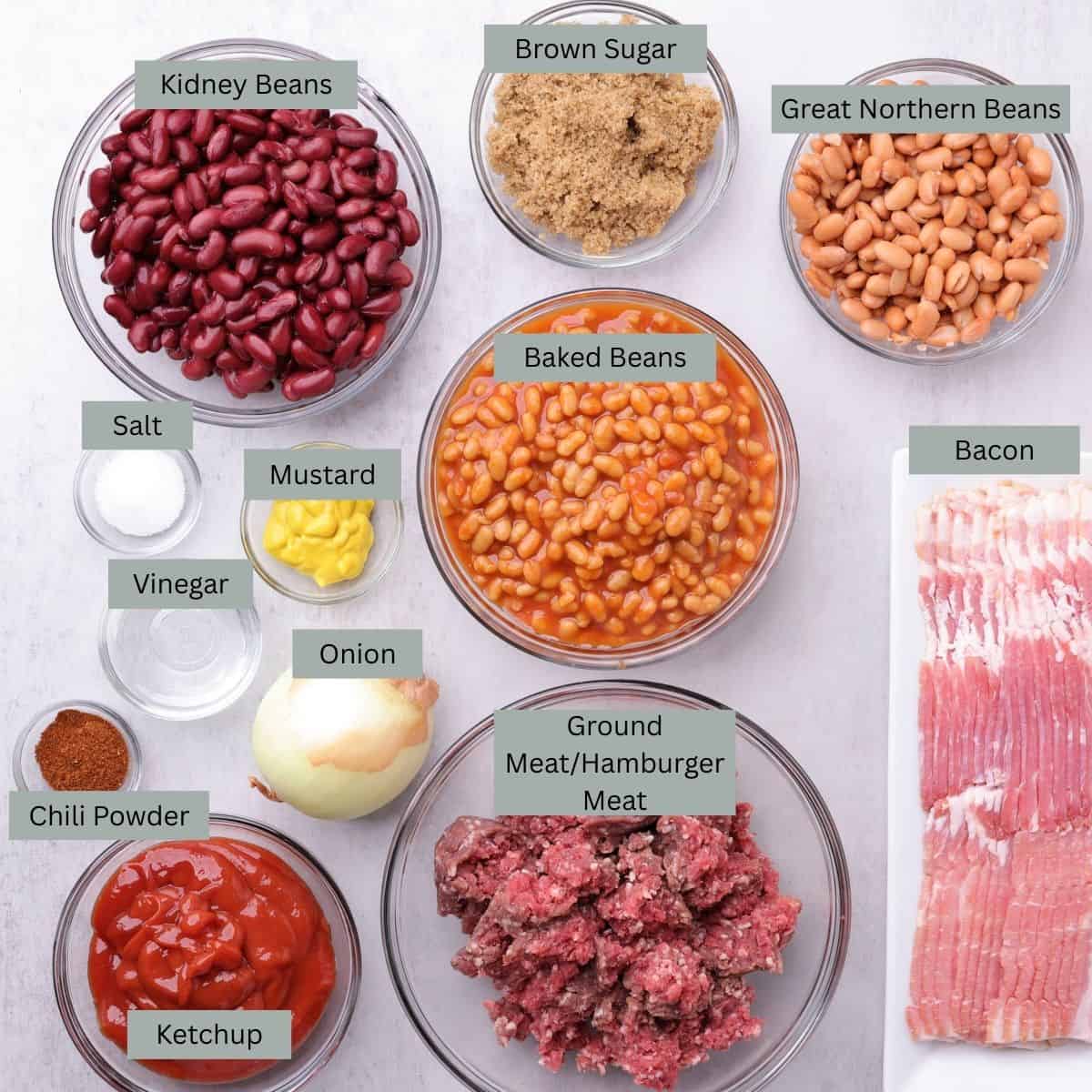 A visual display of the ingredients for Baked Beans with Hamburger and Bacon - kidney beans, baked beans, great northern beans, bacon, ground meat, brown sugar, ketchup, onion, mustard, vinegar, salt and chili powder - each in their own bowl.