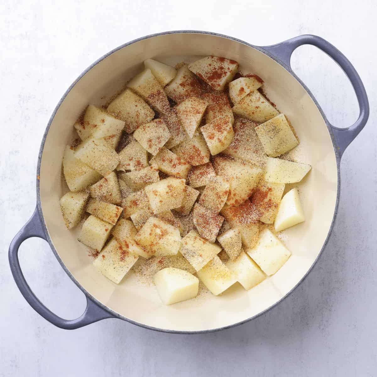 Parboiled potatoes drained and in a cast iron pot covered in seasonings.