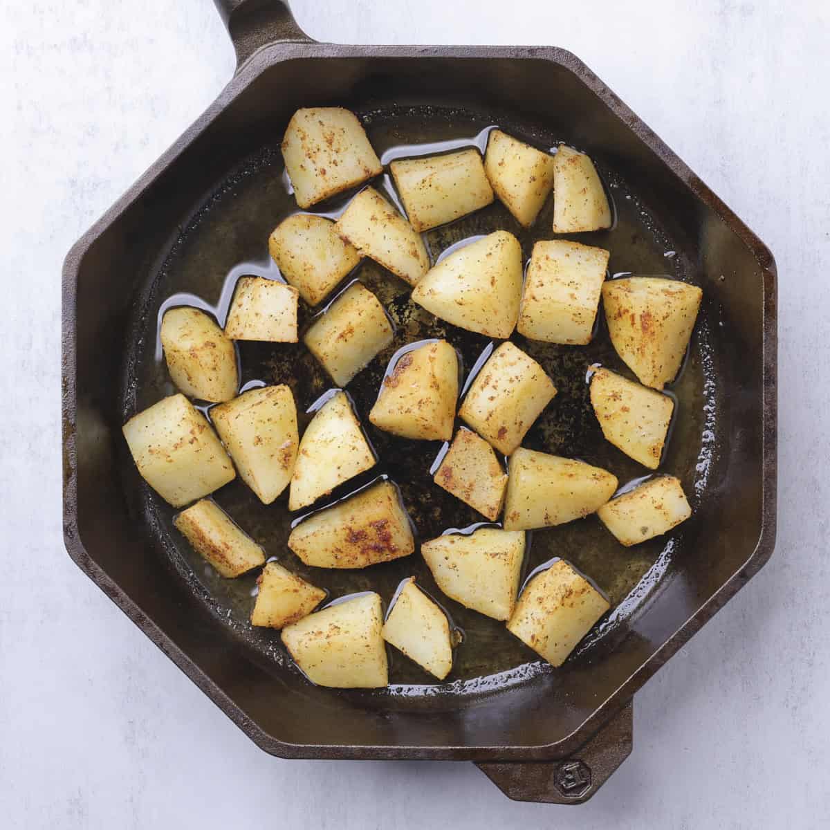 A skillet with seasoned, parboiled potatoes spaced out in the hot oil.