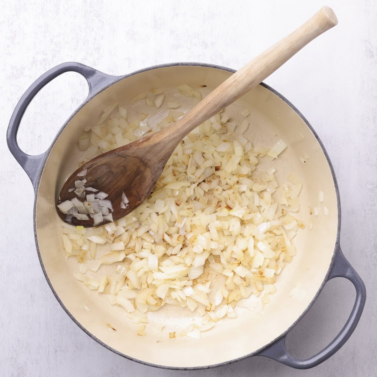 A cast iron pot with sauteed onions and a wooden spoon.
