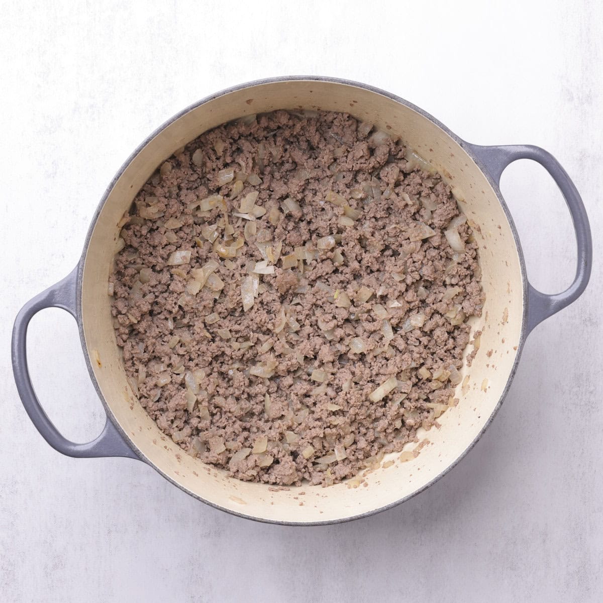 A cast iron pot with browned meat and onions.