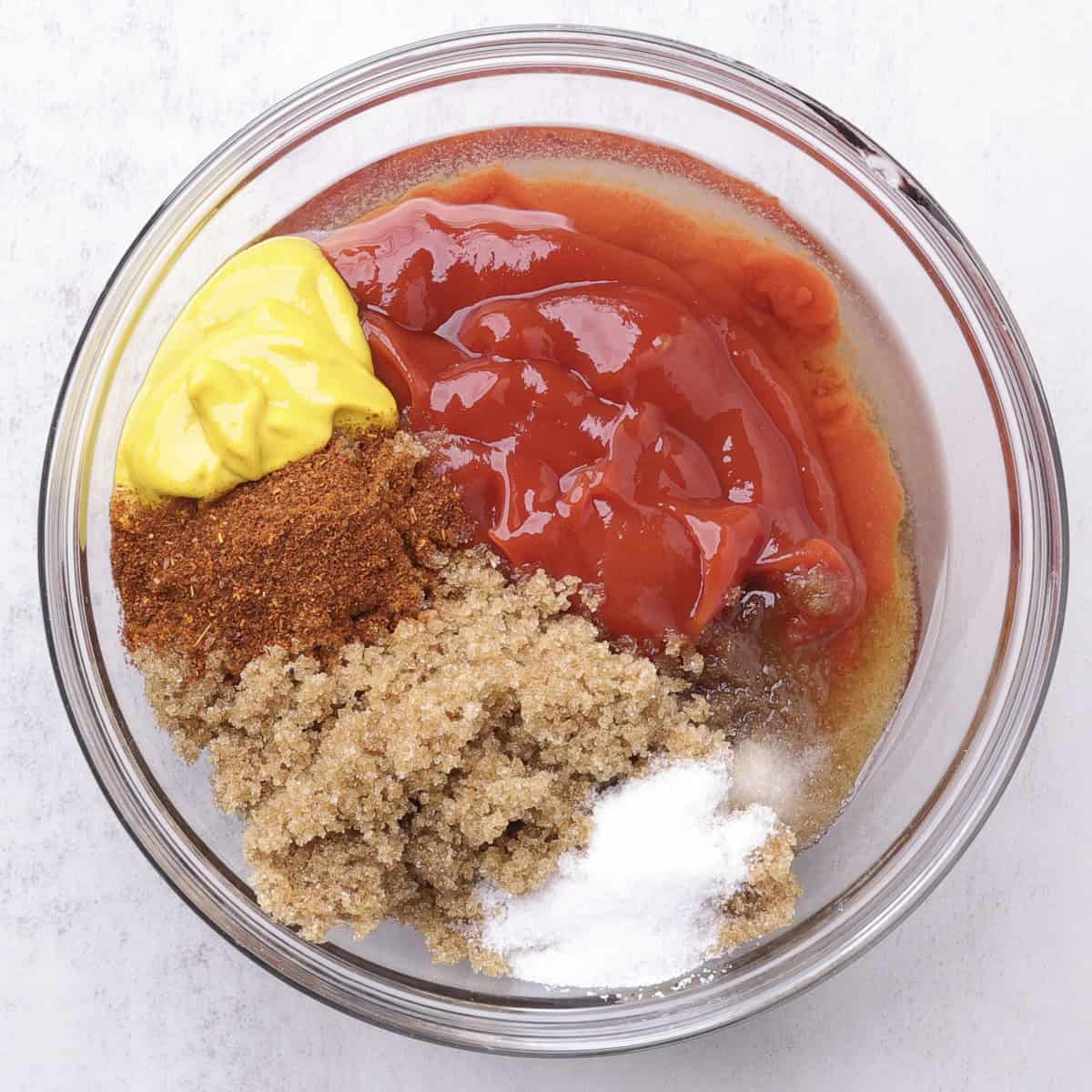 A glass bowl with all the ingredients needed for the Baked Beans with Hamburger and Bacon sauce.