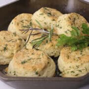 A skillet with baked laminated biscuits, garnished with rosemary and parsley with one turned on it's side.