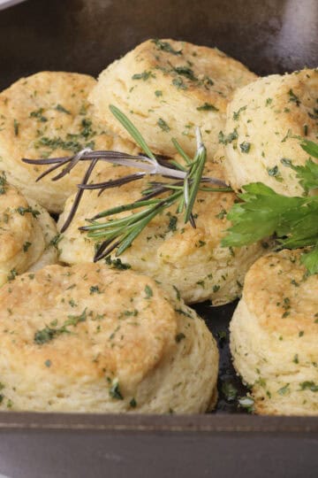 A skillet with baked laminated biscuits, garnished with rosemary and parsley with one turned on it's side.