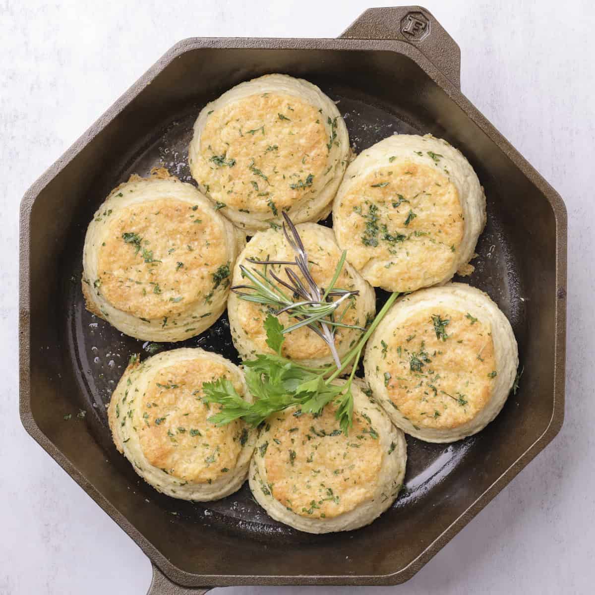 A skillet with the baked biscuits, topped with garlic butter and garnished with parsley and rosemary.