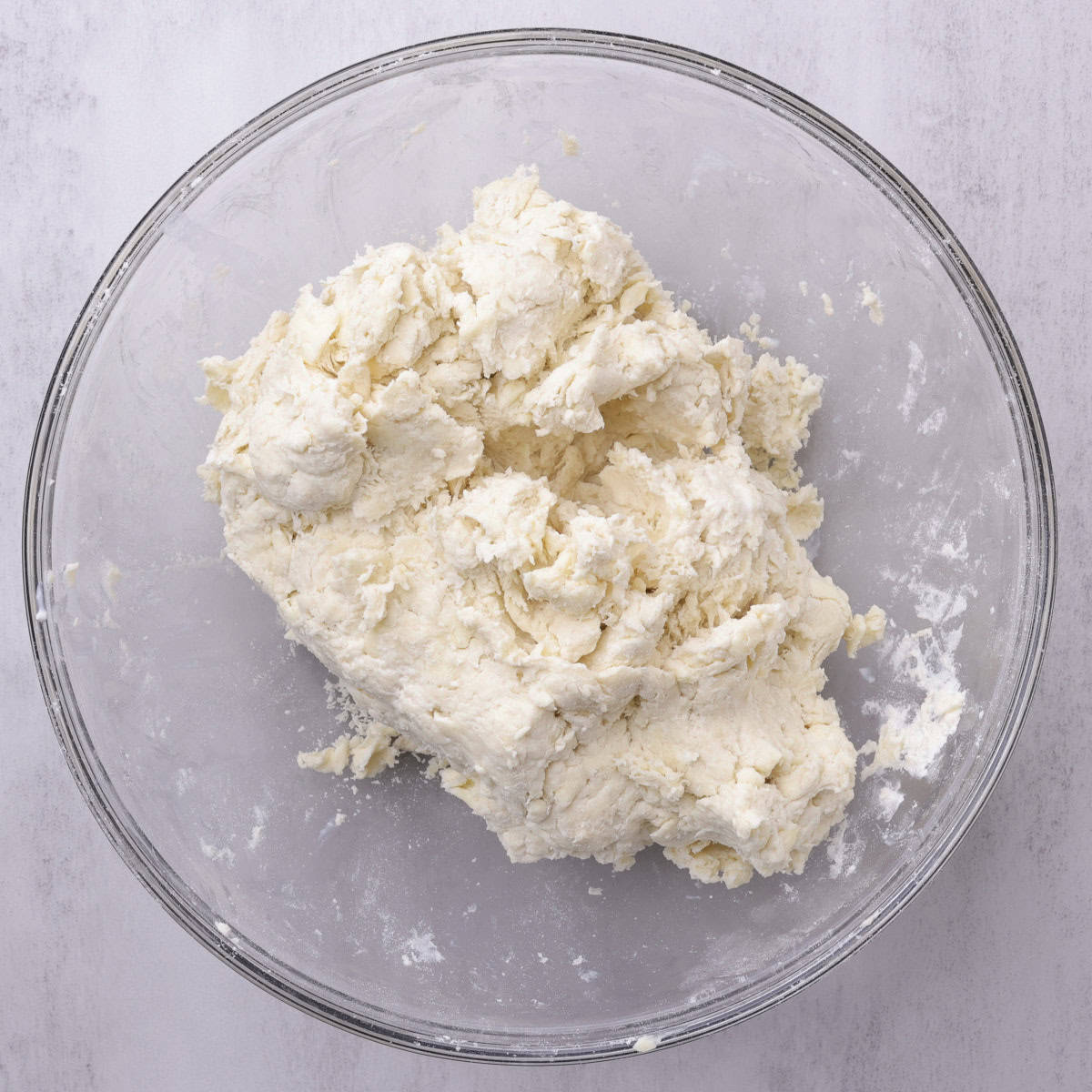 A glass bowl with the batter combined into a shaggy dough.
