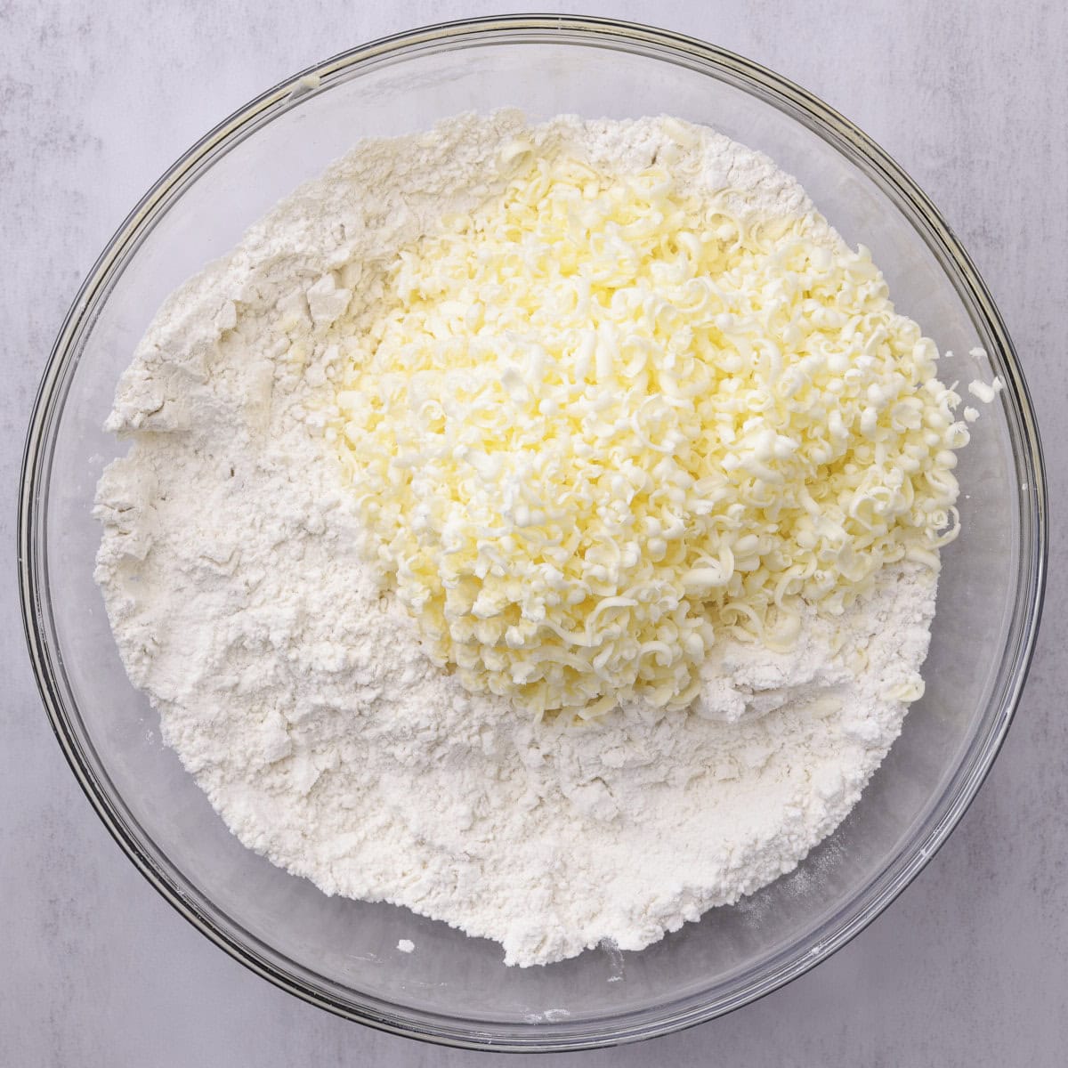 A glass bowl with the butter grated on top of the dry ingredients.