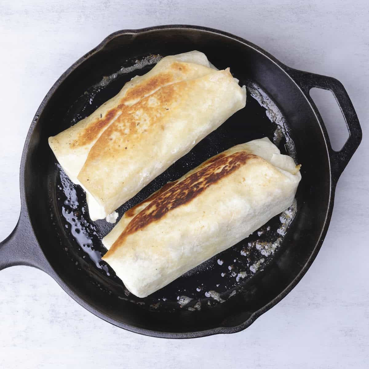 A skillet with two burritos browning in it.