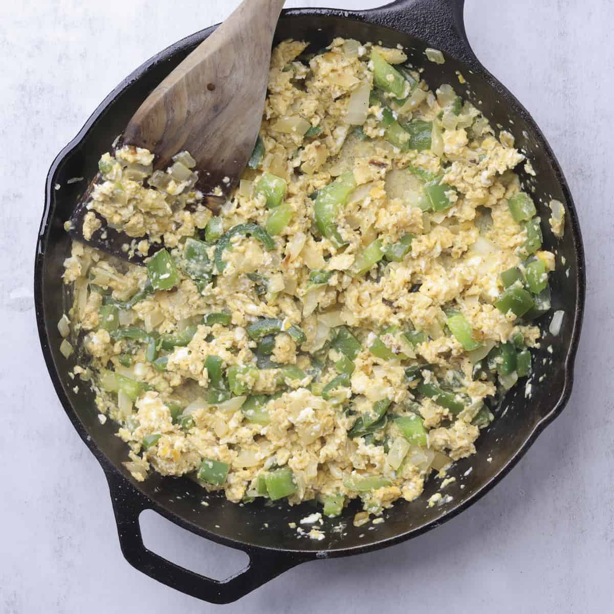 A skillet with sauteed veggies and scrambled eggs.