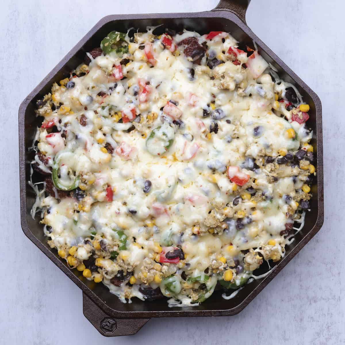 A cast iron skillet with the completed chorizo hash in it, covered in melted cheese.