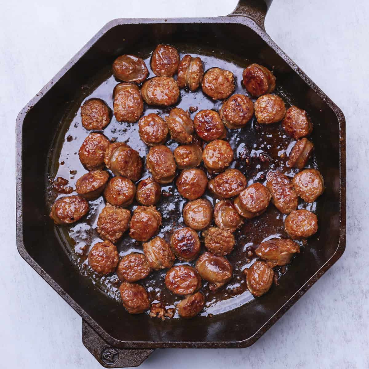 A cast iron skillet with cooked sausage pieces in it.
