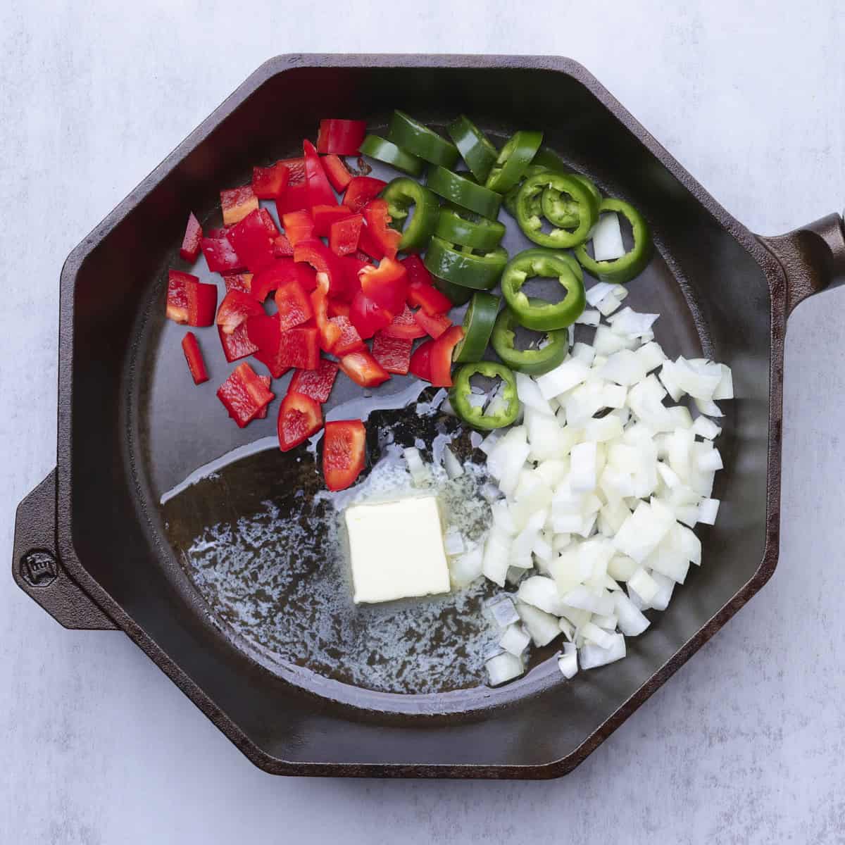 A skillet with melted butter and chopped jalapenos, red bell peppers and onions in it.
