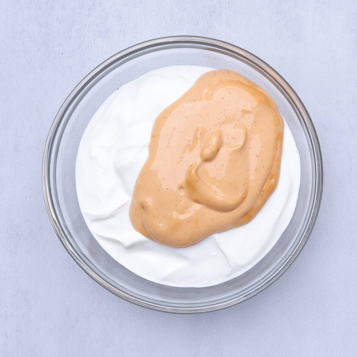 A glass bowl with sour cream and chipotle aioli in it, ready to combine.