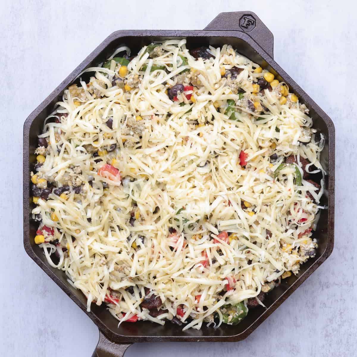 A skillet with the assembled hash in it, topped with shredded cheese.