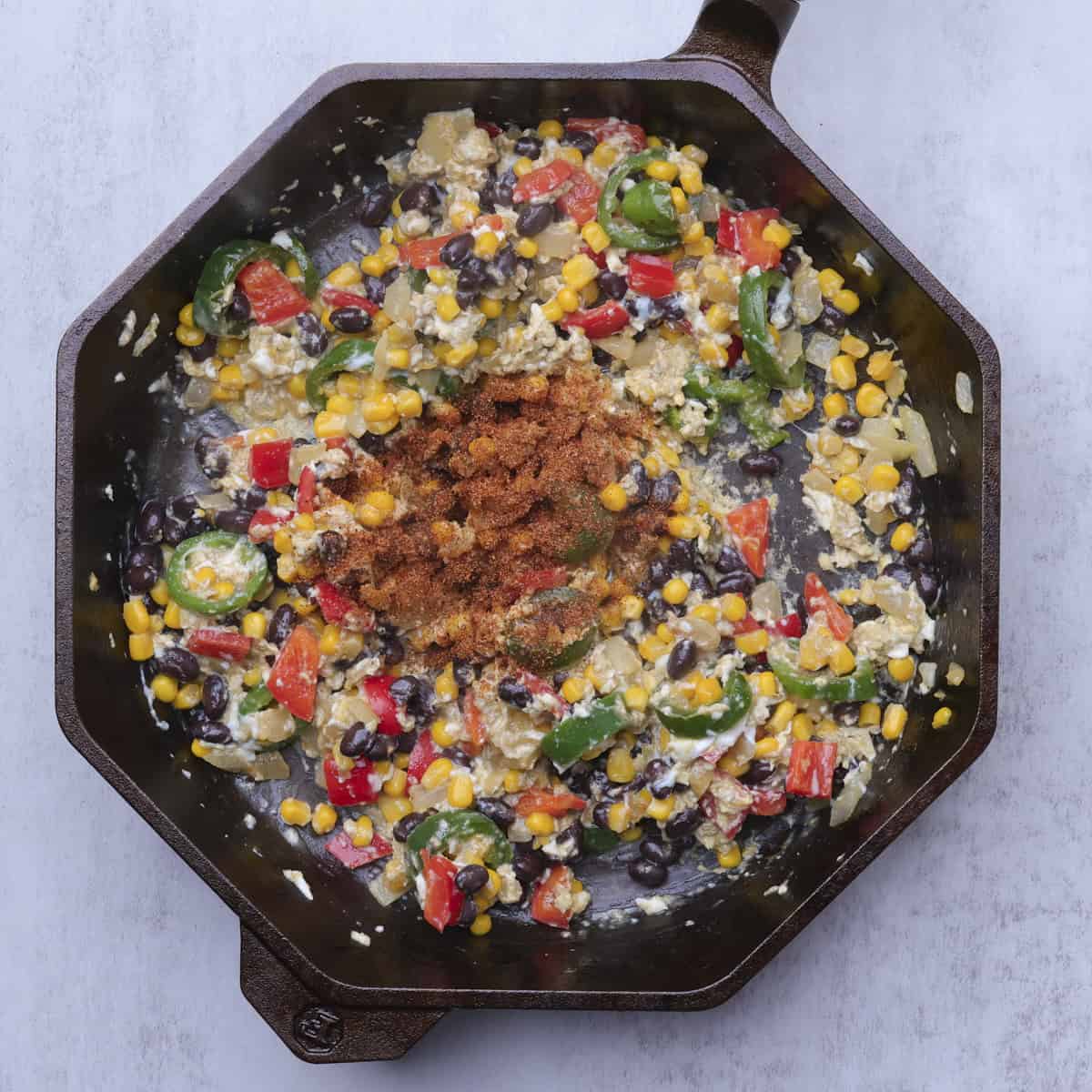A cast iron skillet with the sauteed vegetables, scrambled eggs and blackened seasoning sprinkled on top.