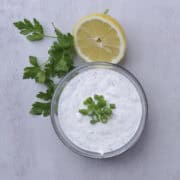 A bowl of Dill Dip garnished with green onions and displayed with half a lemon and parsley.
