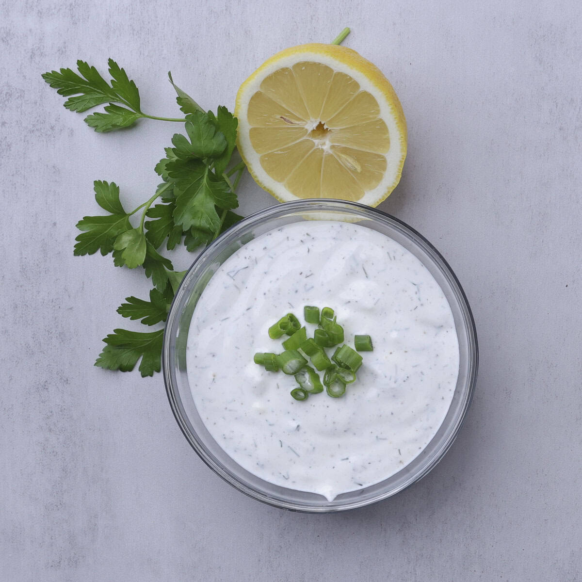 A bowl of Dill Dip garnished with green onions and displayed with half a lemon and parsley.