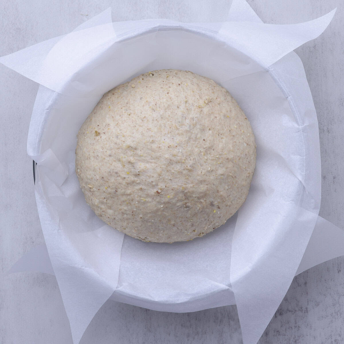 A ball of dough in a bowl lined with parchment paper.