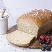 A sandwich loaf of seeded bread sliced and displayed on a wooden board with berries and a jar of honey.