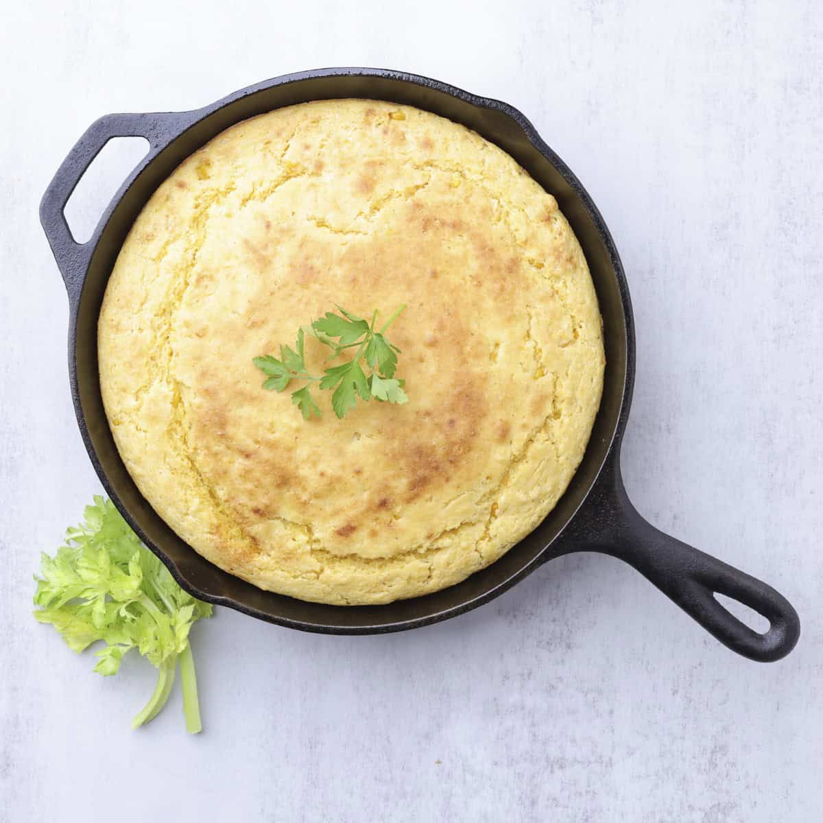 A golden brown baked skilled of Corn Bread with Creamed Corn garnished with greens.